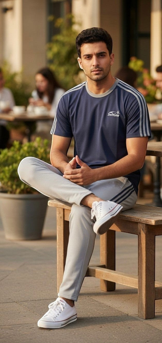 Swift Gear navy blue short-sleeve t-shirt with grey trim and triple stripe accents, paired with light grey track pants. Model is sitting outdoors.
